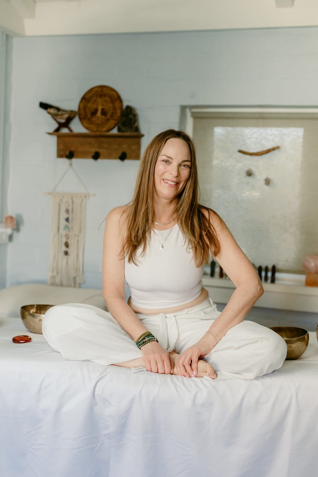 Miki sitting cross legged on the treatment table beside a set of singing bowls